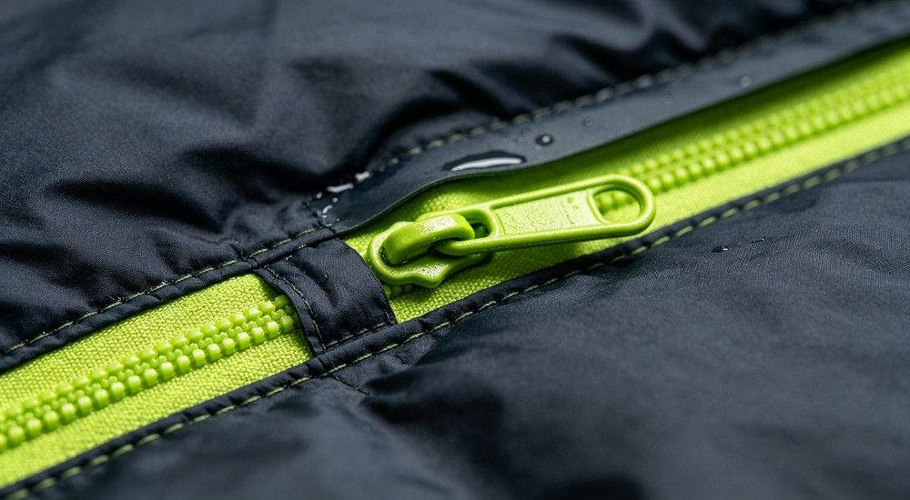 Close‑up view of durable green anti‑snag zipper on sleeping bag fabric, fine stitching detail, outdoor camping gear component, macro product photography