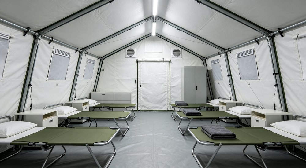 Interior view of a spacious emergency relief tent showing adequate headroom natural lighting through windows and organized living space for displaced family accommodation