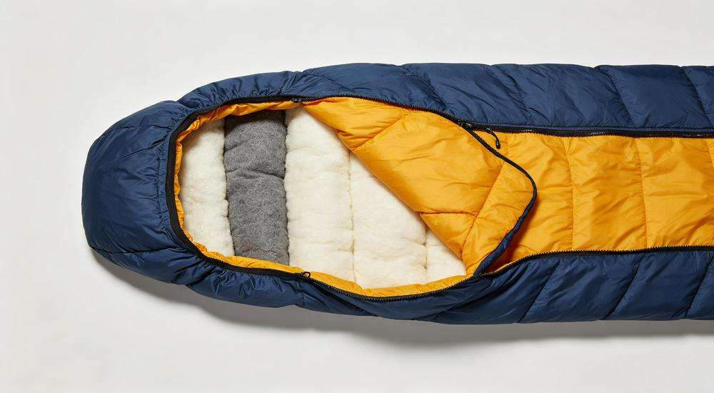 Top view cross section of sleeping bag showing layers: outer shell fabric, insulation filling, inner lining, material composition display, studio lighting