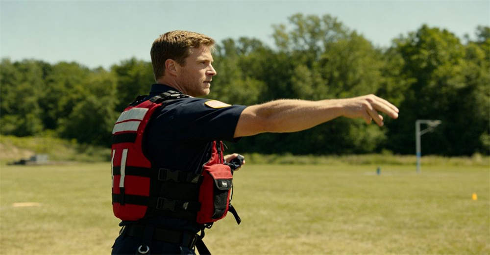 Training shot of rescuer in correct throw bag throwing stance holding orange bag ready to launch with feet apart showing real-world deployment conditions and team coordination